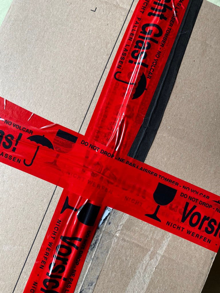 Paket zugeklebt mit dem roten „Vorsicht Glas!“-Klebeband.
